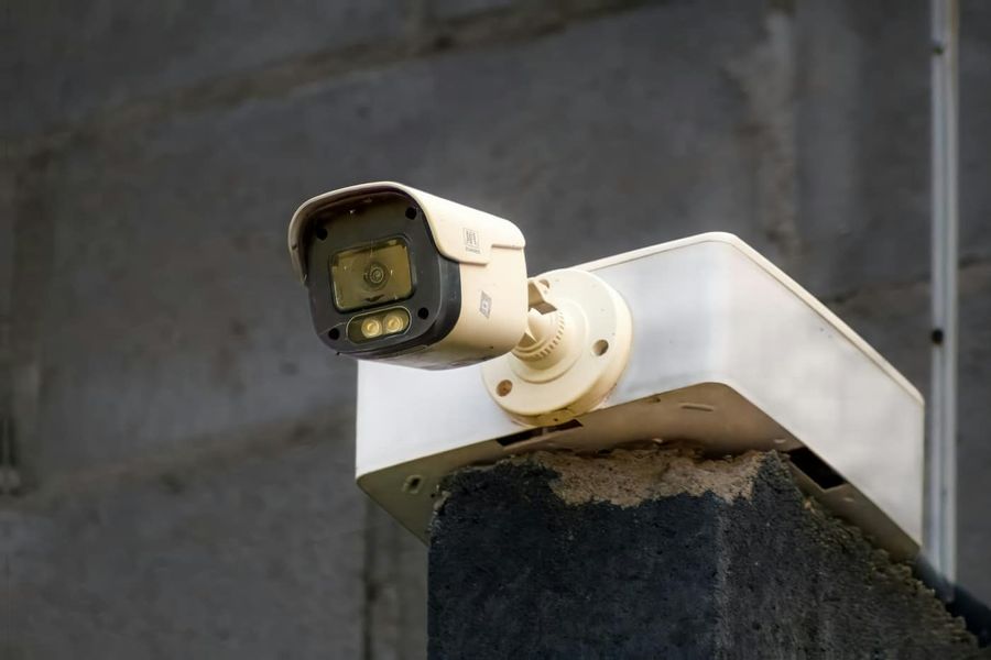 Biała kamera monitoringu zamontowana na murze przy wejściu