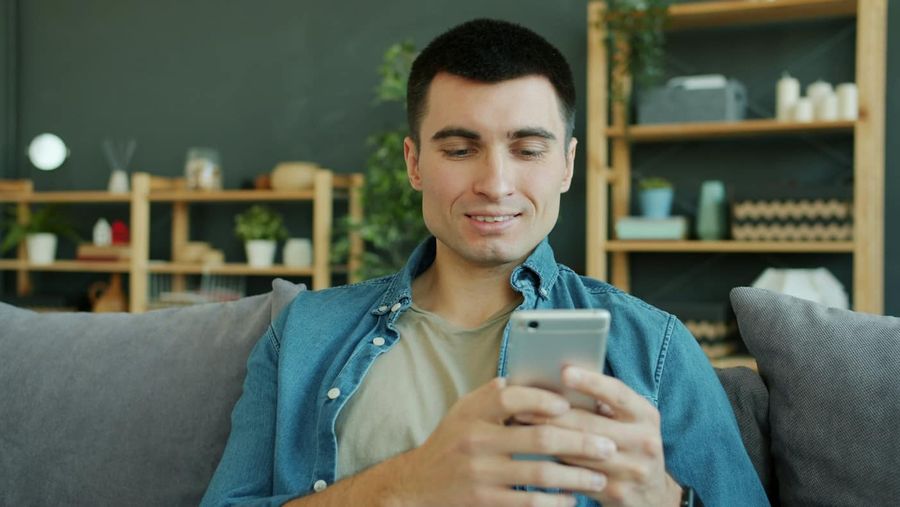 Uśmiechnięty mężczyzna na kanapie przegląda telefon