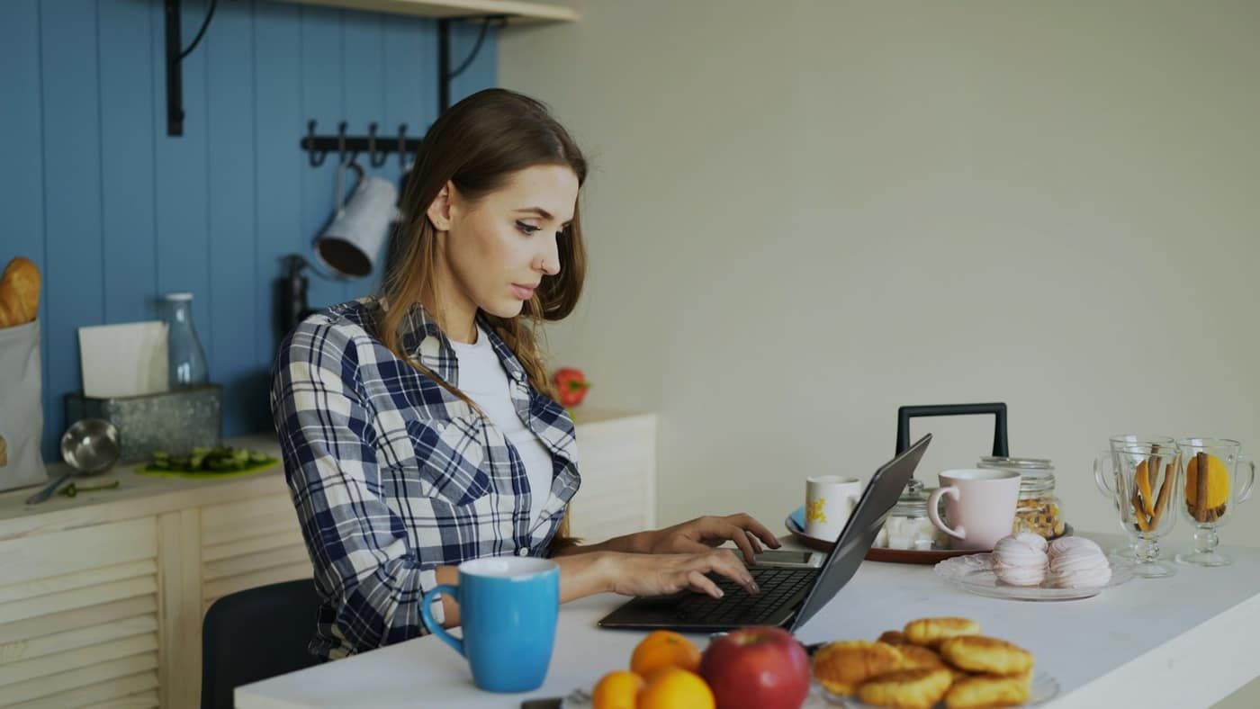 Kobieta pracująca na laptopie przy stole w jasnej kuchni