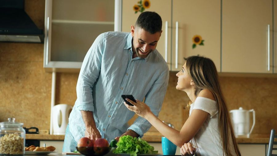 Para w kuchni, kobieta pokazuje mężczyźnie coś na telefonie