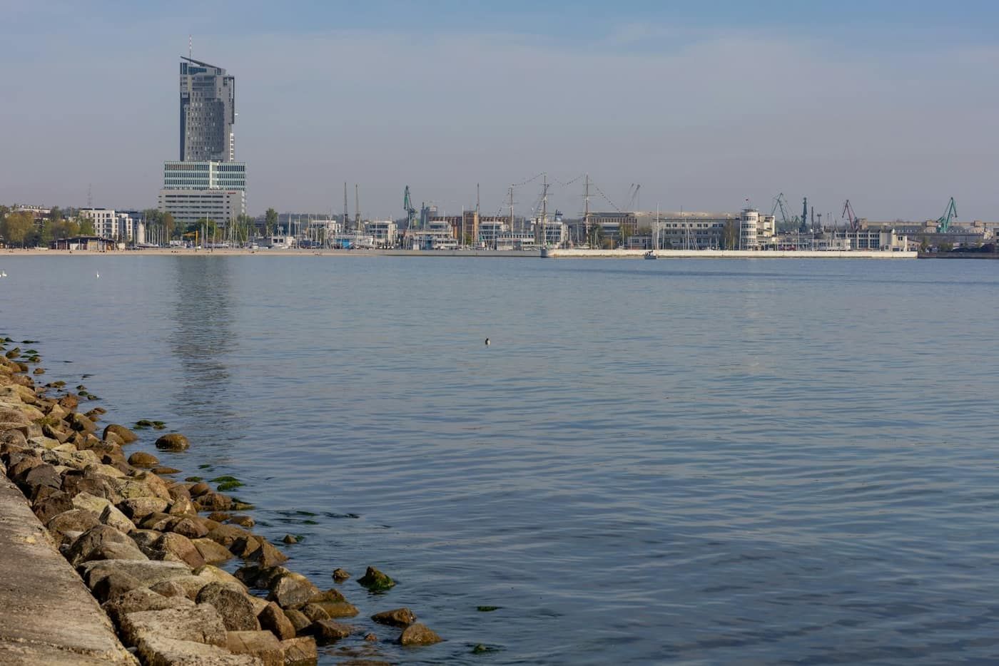 Zatoka Gdańska z kamiennym nabrzeżem, w tle panorama Gdyni z wysokim wieżowcem