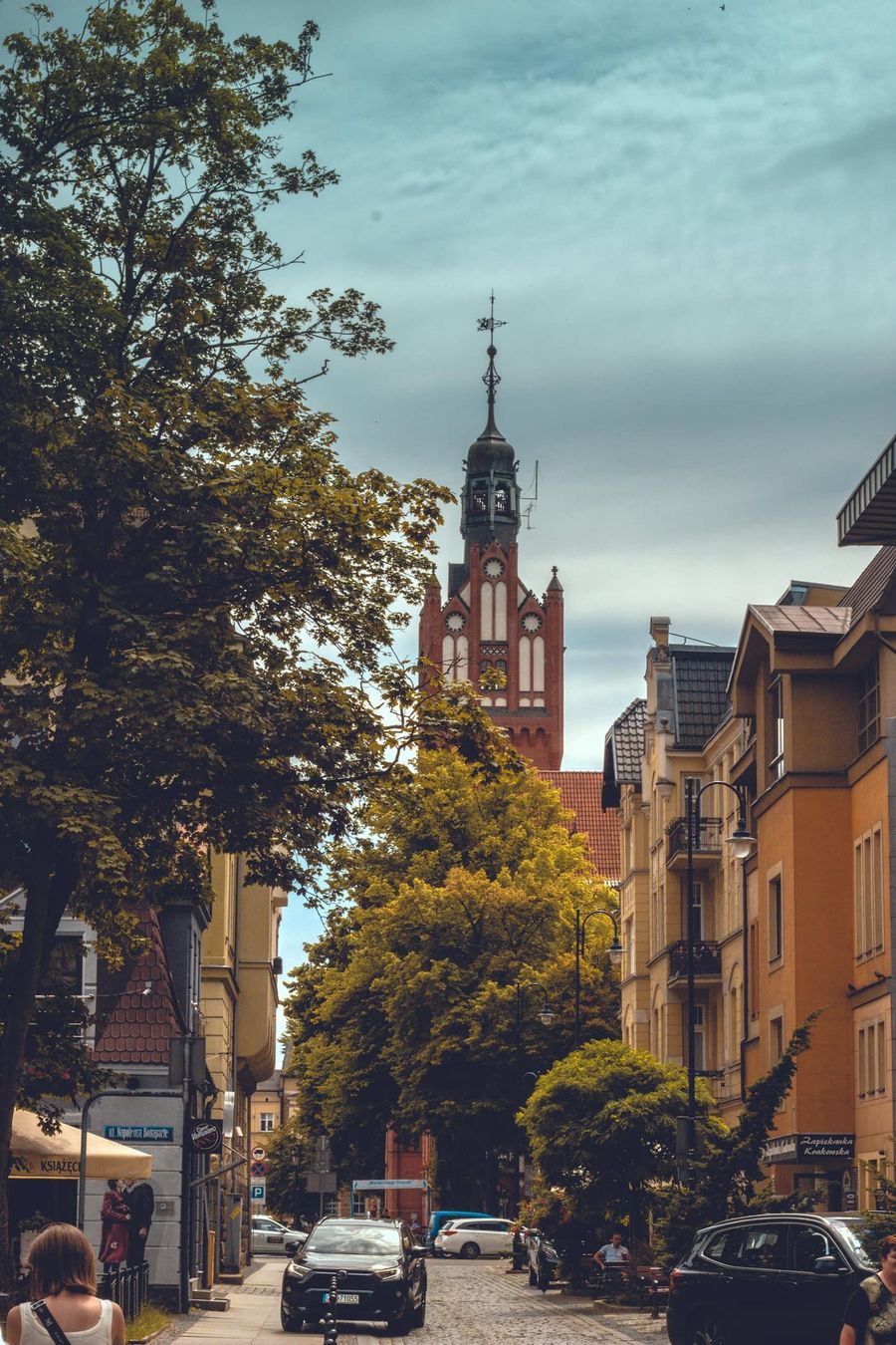 Ulica w Słupsku z drzewami i kamienicami, w tle neogotycka ceglana wieża