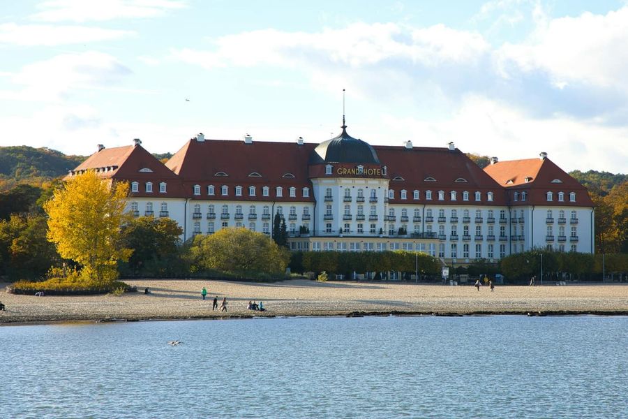 Zabytkowy hotel z czerwonym dachem nad plażą w Sopocie, na pierwszym planie woda